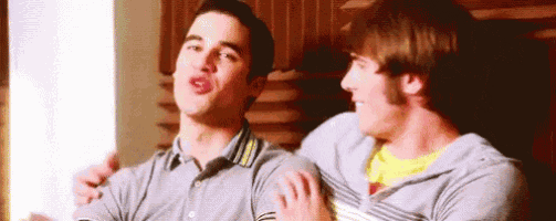 two young men are sitting next to each other in a room and laughing .