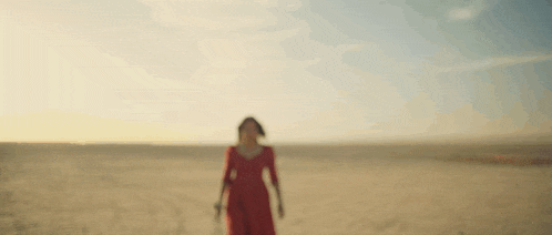 a woman in a red dress is walking through the desert .