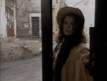 a woman wearing a hat is standing in front of a window with a bicycle in the background