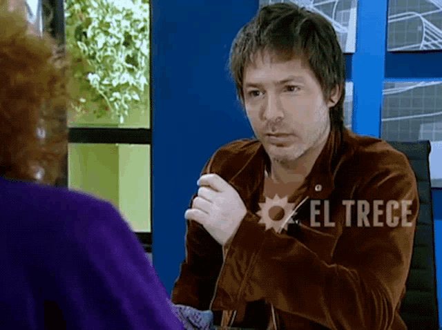 a man in a brown jacket is talking to a woman with el trece written on his jacket