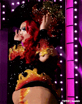 a drag queen with red hair is standing in front of a pink wall with lights behind her
