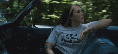 a woman is sitting in a car wearing a t-shirt that says burst / glow