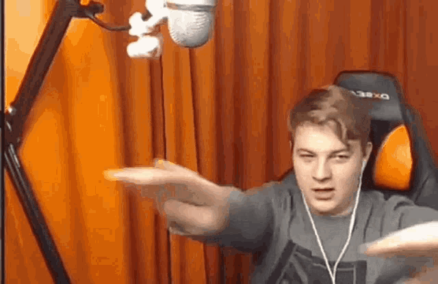 a young man is sitting in a chair in front of a microphone and making a funny face .