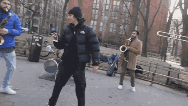 a man in a black north face jacket stands in front of a saxophone player