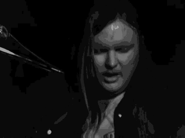 a black and white photo of a woman singing into a microphone in a dark room .