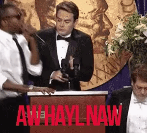a man in a tuxedo stands at a podium with aw hayl naw written on it