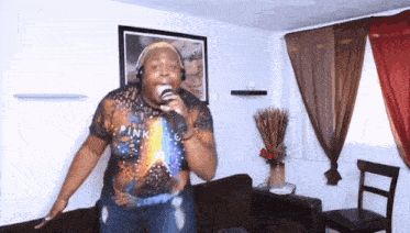a man singing into a microphone in a living room wearing a pink floyd shirt