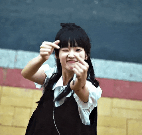 a young girl is making a heart shape with her hands and smiling .