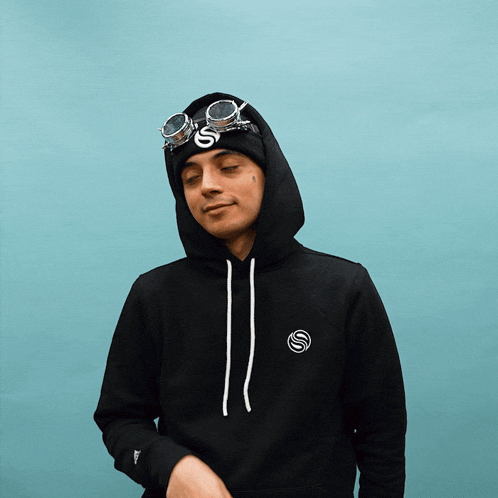 a man wearing a black hoodie and goggles has the letter s on his head