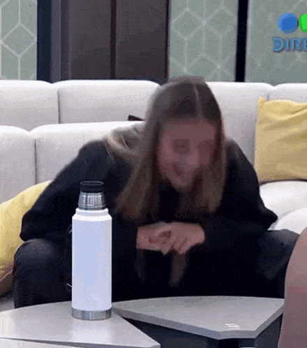 a woman sits on a couch with a bottle of water on a table in front of her