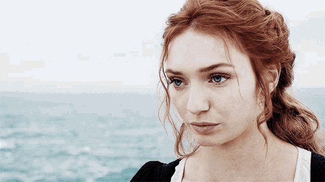 a woman with red hair and blue eyes is looking at the ocean