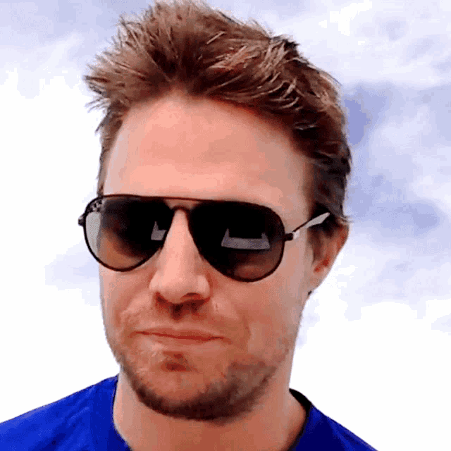 a close up of a man wearing sunglasses with a blue shirt