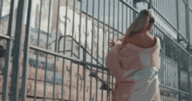 a woman in a pink dress is standing next to a fence .