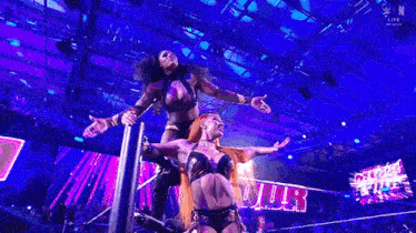 a couple of women are standing on top of a pole in a wrestling ring .