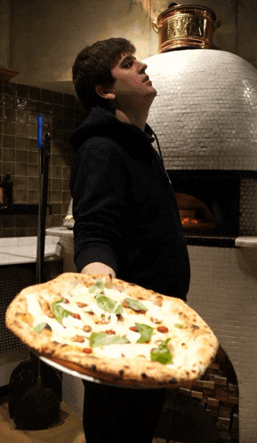 a man in a black hoodie is holding a pizza in front of a pizza oven