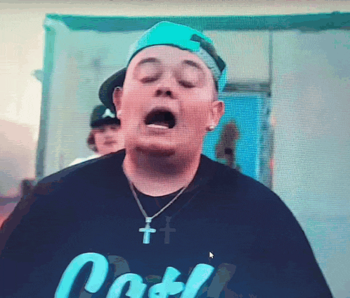 a man wearing a hat and a necklace with a cross on it has his mouth open