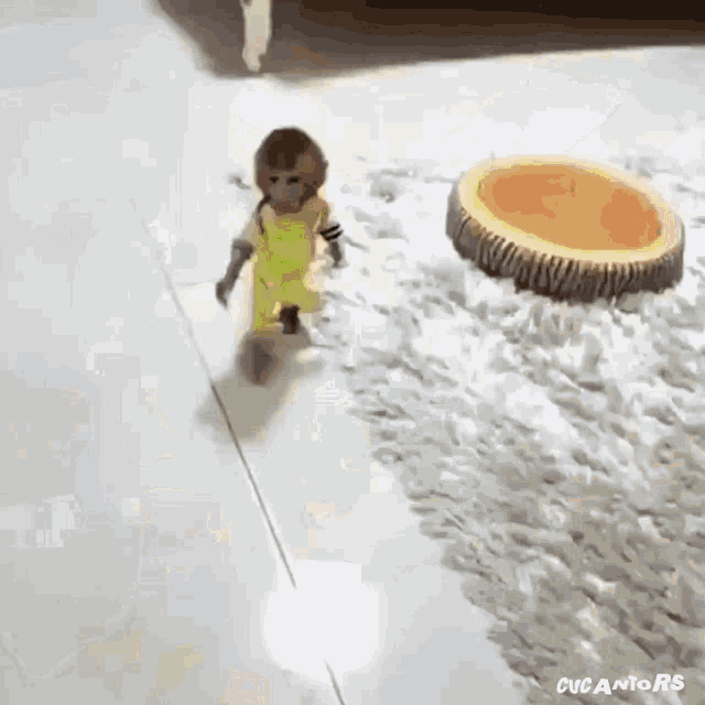 a small monkey in a yellow jumpsuit is walking on a white tiled floor .