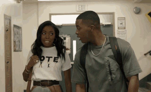 a man and a woman are standing next to each other in a hallway with an exit sign above them