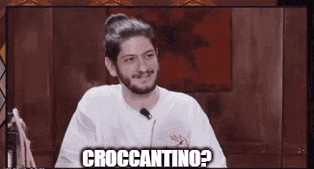 a man with a beard is sitting in front of a microphone with the words croccantino written above him .