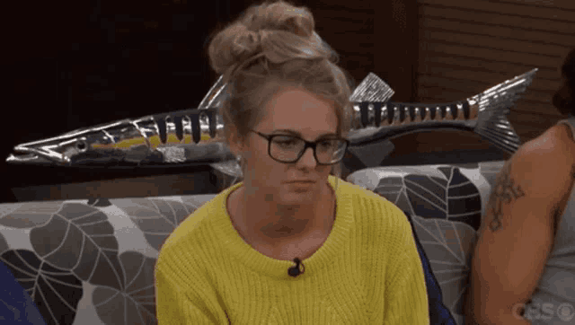 a woman wearing glasses and a yellow sweater sits on a couch in front of a cbs logo