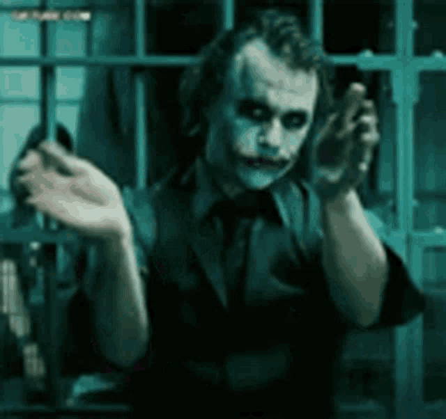 a man dressed as the joker is standing in a dark room with his hands outstretched .