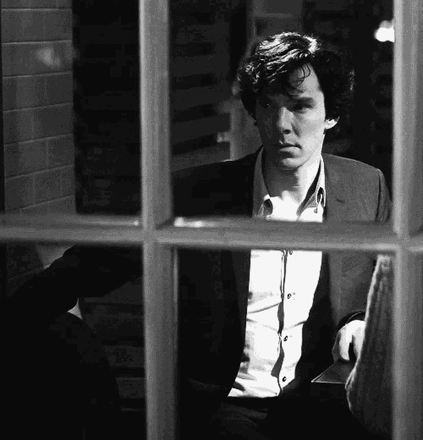 a black and white photo of a man in a suit looking out a window