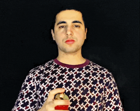 a man wearing a patterned shirt is spraying a red bottle of perfume