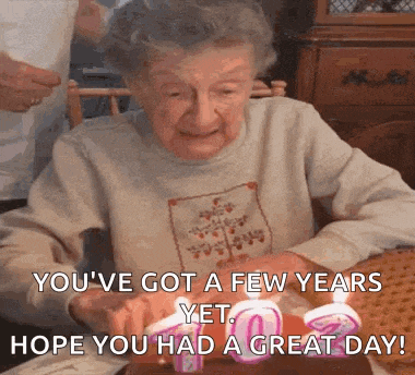 an elderly woman is sitting at a table with candles and a birthday message .