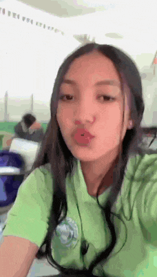a girl in a green shirt is blowing a kiss while taking a selfie .