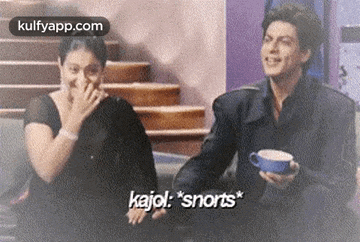 a man and a woman are sitting on a couch and laughing . the man is holding a cup of coffee .