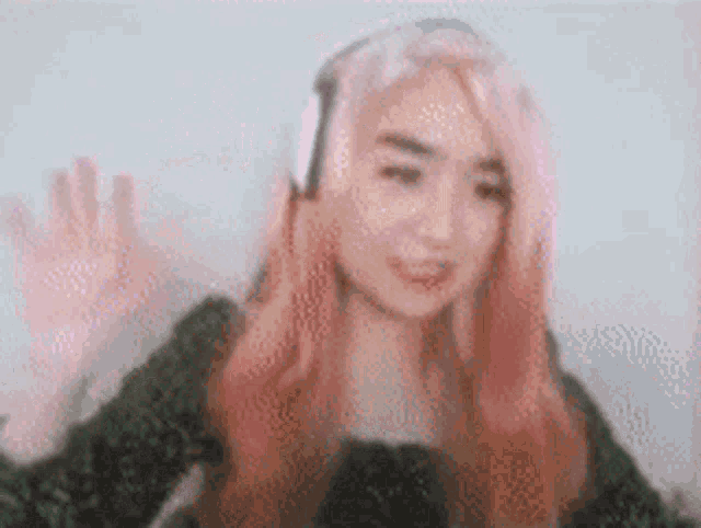 a woman with pink hair wearing headphones is waving her hand .