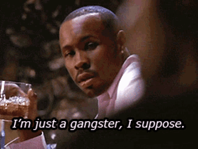 a man in a pink shirt is holding a glass and says " i 'm just a gangster i suppose "
