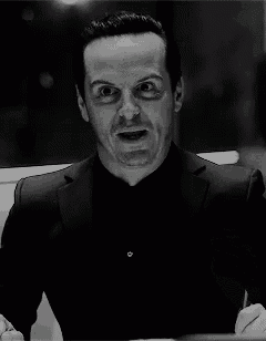a black and white photo of a man in a suit and black shirt making a funny face .