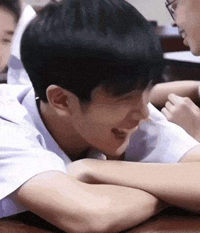 a group of young men are sitting at a table with their arms crossed and one of them is smiling .