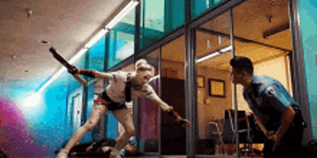harley quinn is fighting a police officer in a hallway while holding a bat .