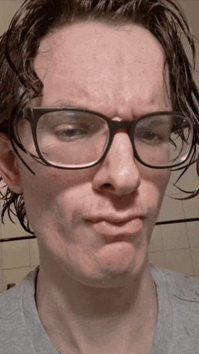 a man wearing glasses and a gray shirt makes a face