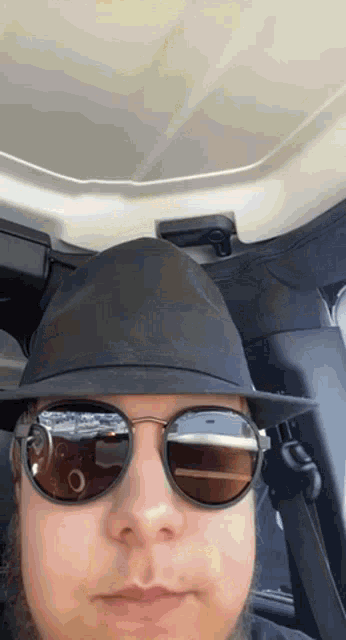 a man wearing a hat and sunglasses is driving a car .