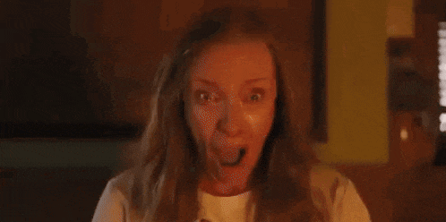 a close up of a woman with long blonde hair making a funny face in a dark room .