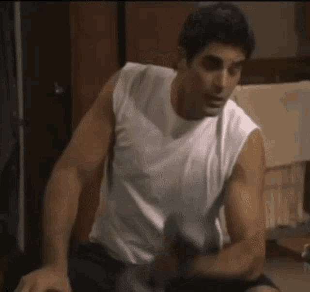 a man in a white tank top sits on a chair
