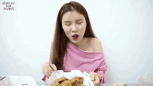 a woman in a pink and white striped top eating fried chicken
