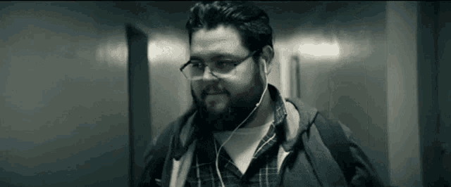 a man with a beard and glasses is wearing headphones and walking down a hallway .