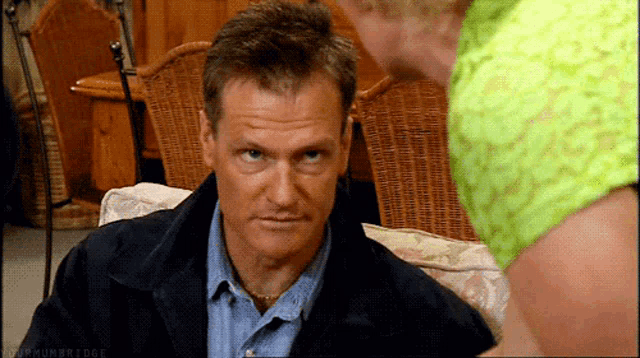 a man sitting on a couch with a woman in a green shirt behind him and a watermark that says my humbridge