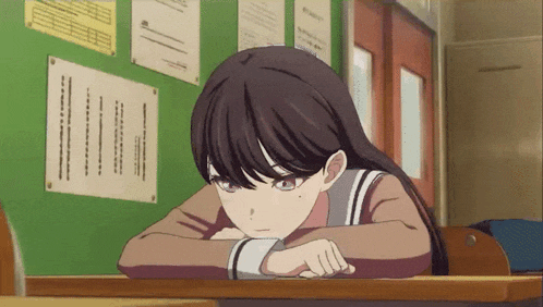 a girl leaning her head on a desk in front of a green wall