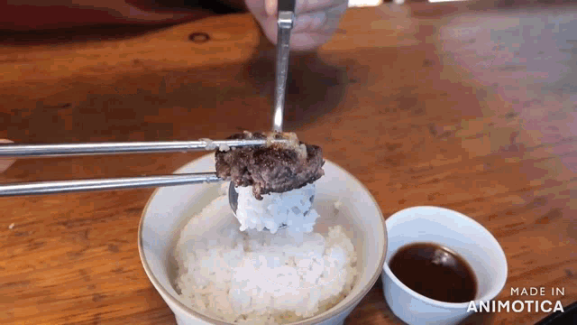 a person is holding a piece of meat over a bowl of rice .