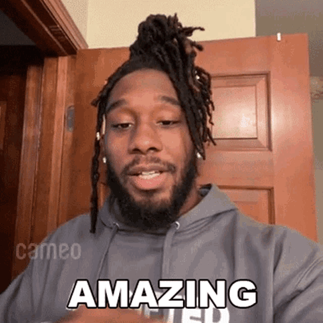 a man with dreadlocks is wearing a grey hoodie that says amazing