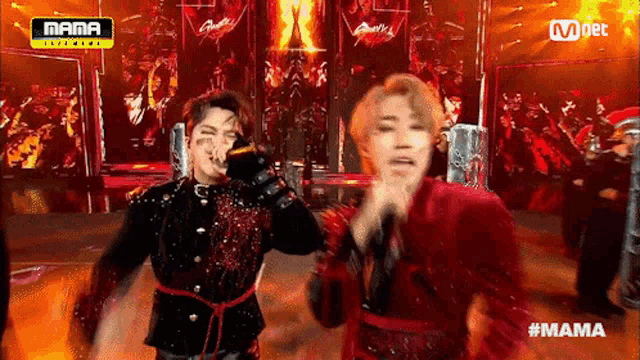 two men are singing into microphones on a stage in front of a sign that says mama .