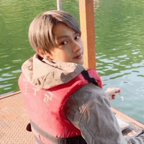 a young man wearing a life jacket is sitting on a dock next to a lake .