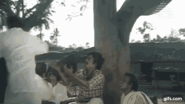 a group of people are sitting under a tree and talking to each other .