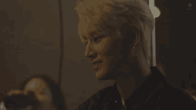 a man with blonde hair is smiling in a dark room while a woman looks on .