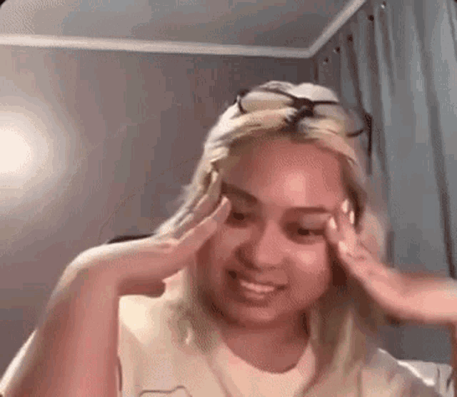 a woman wearing glasses is smiling and holding her head in a room .